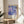 A framed poster of a colorful abstract floral design hangs on a wall in a room with a wooden table and a white chair.