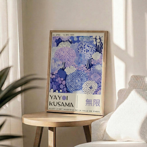 A framed poster of a colorful abstract floral design hangs on a wall in a room with a wooden table and a white chair.