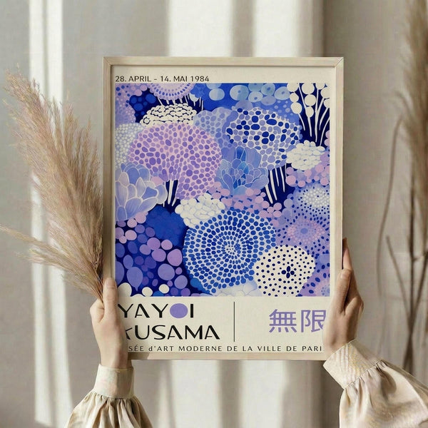 A person is holding up a framed poster with a vibrant abstract design featuring various shapes and patterns in shades of blue, purple, and white.