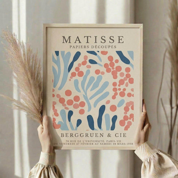 A person is holding up a framed poster of the Métisse art movement, featuring a floral pattern in shades of blue, pink, and orange.