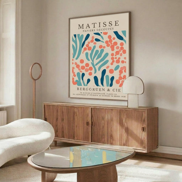 a living room with a large poster of the Motsie poster hanging on the wall above a wooden cabinet. The poster has a colorful abstract design with orange and blue shapes. The room also includes a white sofa, a glass coffee table, and a lamp on a side table.