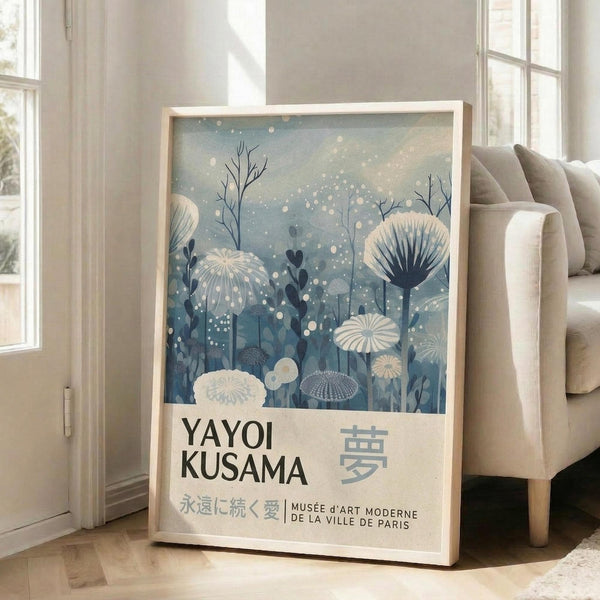 A framed poster of a floral design with the text "YAYOI KUSAMA" and "MUSEÉE J'ART MODERNE DE LA VILLE DE PARIS" printed on it, placed on a wooden floor next to a couch.