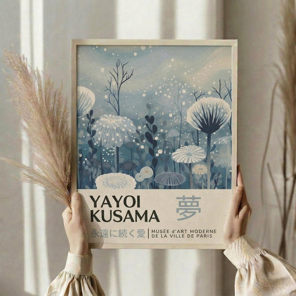 A person is holding up a framed poster with a floral and nature-inspired design, featuring the text "YAYOI KUSAMA" and "MUSÉ H'ART MODERNE DE LA VILLE DE PARIS" on it.