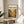 a framed poster of Pollock's painting titled "Chaos and creativity" displayed on a wooden table in a room with a white chair and a plant in the background.