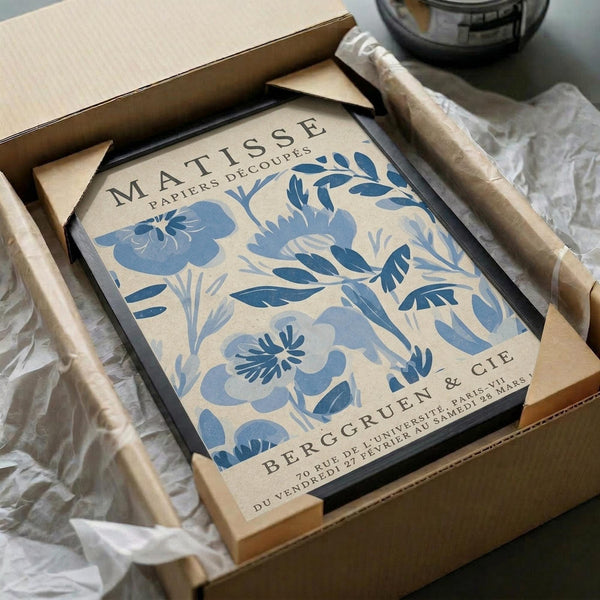 a framed poster of a blue floral design, which appears to be a piece of artwork. The poster is placed in a cardboard box, and there is some wrapping paper visible around it.