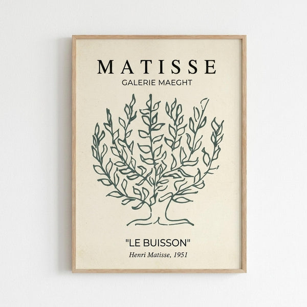 A minimalist botanical line drawing in dark green on cream paper, featuring a stylized bush or shrub with delicate branching stems and small leaves. The artwork is displayed in a light wood frame against a white wall. Text at the top reads "MATISSE" and "GALERIE MAEGHT" in black letters, with "LE BUISSON" and "Henri Matisse, 1951" below the illustration. The simple, elegant design captures Matisse's characteristic fluid line work in an exhibition poster style.