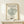 May include: Framed art print displaying a simple line drawing of a leafy bush or tree in dark green on cream background, with "MATISSE GALERIE MAEGHT" and "LE BUISSON" text above and below. Light wood frame sits on white wooden shelf against cream wall, with small wrapped gift box nearby.