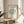 May include: Framed botanical art print featuring green line drawing of a leafy bush or tree on cream background with black text reading "MATISSE GALERIE MAEGHT" and "LE BUISSON Henri Matisse, 1951". Print displayed in light wood frame on round wooden side table next to beige upholstered chair, with plant leaves visible in corner and natural sunlight casting shadows on white wall.