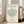 May include: Framed botanical art print featuring a stylized green tree illustration on cream background, displayed in light wood frame against white wall in bright living room with beige sofa and large windows. Modern minimalist home decor setting with natural lighting casting soft shadows on hardwood floors.