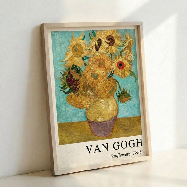 May include: Framed reproduction of Van Gogh's famous sunflowers painting in natural wood frame, leaning against white wall. Artwork shows vibrant yellow sunflowers in ceramic vase against turquoise background, with text reading "VAN GOGH 'Sunflowers, 1888'" at bottom. Visible brushstroke texture and warm golden tones throughout the floral still life composition.