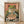 May include: Framed vintage-style Japanese poster showing a green frog with orange eyes eating ramen noodles with chopsticks from a red and teal bowl, set against a coral pink background with Japanese text, displayed in a light wood frame leaning against a white wall on light wooden flooring.