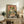 May include: Framed vintage-style Japanese poster featuring a green frog with large orange eyes eating noodles from a red and teal ramen bowl, holding chopsticks, with Japanese text on coral pink background. Wooden frame displayed on rustic wood sideboard next to fern plant, books, and ceramic vase in modern living room setting with beige chair visible.