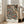 May include: Framed botanical art print with intricate dark teal background featuring ornate floral pattern in cream, coral, and rust tones. Shows detailed roses, chrysanthemums, and flowing leaves in Victorian decorative style. White matted frame leans against wall near beige upholstered chair in bright, naturally-lit living room with white walls and large windows.