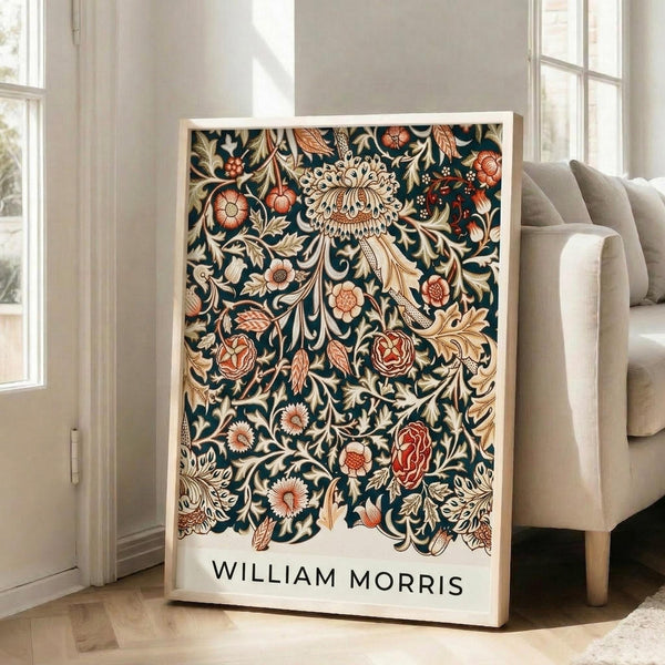 May include: Framed botanical art print with intricate dark teal background featuring ornate floral pattern in cream, coral, and rust tones. Shows detailed roses, chrysanthemums, and flowing leaves in Victorian decorative style. White matted frame leans against wall near beige upholstered chair in bright, naturally-lit living room with white walls and large windows.