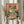 May include: Person holding framed vintage-style Japanese poster featuring green frog with orange eyes eating noodles from a ramen bowl using chopsticks, with Japanese text on coral-colored background. Light wooden frame, held against white curtained window with dried wheat stems visible to the left.