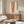 May include: Framed art print featuring a figure study in red and beige tones hanging above a wood credenza in a modern living room. The artwork shows partial human form rendered in warm reddish hues against cream background. Room styled with white curved chair, glass coffee table, and contemporary lighting fixtures on neutral walls.