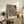 May include: Framed botanical art print with intricate dark navy background featuring ornate floral patterns in cream, coral, and gold tones. The vintage-style design shows detailed leaves, roses, and decorative motifs. Display shows rustic wooden sideboard with books, ceramic vases, fern plant, and beige upholstered chair in warm, neutral-toned room setting.