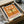 May include: Orange vintage-style dragonfly poster displayed in wooden frame inside cardboard shipping box with tissue paper. The poster features detailed dragonfly illustration with Japanese text, "DRAGONFLY" and "KYOTO SCIENCE MUSEUM 2005年4月16日" in retro exhibition style design. Warm orange background with cream and green accents, surrounded by protective packaging materials.