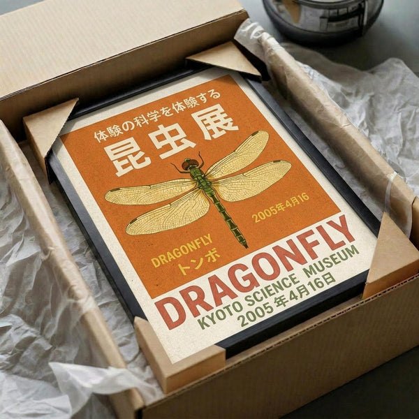 May include: Orange vintage-style dragonfly poster displayed in wooden frame inside cardboard shipping box with tissue paper. The poster features detailed dragonfly illustration with Japanese text, "DRAGONFLY" and "KYOTO SCIENCE MUSEUM 2005年4月16日" in retro exhibition style design. Warm orange background with cream and green accents, surrounded by protective packaging materials.