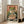 May include: Framed poster print leaning against white wall in bright living room with beige sofa. Artwork shows green cartoon frog with orange eyes eating noodles from red and teal bowl using chopsticks, in Japanese vintage poster style with coral background and white Japanese characters. Print has weathered, distressed texture with black border in light wood frame.