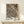 May include: Framed vintage botanical poster featuring William Morris's intricate floral pattern with ornate flowers, leaves, and vines in coral, cream, and gold tones on dark navy background. The print sits on a light wood console table next to a small white wrapped gift with evergreen sprig. The frame appears natural wood against a cream wall.