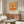 May include: Orange and cream vintage-style dragonfly poster in thin frame hanging above mid-century walnut credenza in modern living room. Poster features detailed green dragonfly illustration with Japanese text. Room has cream upholstered chair, brass floor lamp, oval glass coffee table, and neutral decor creating minimalist aesthetic.