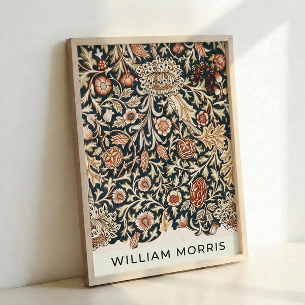 May include: Framed botanical art print leaning against white wall, featuring intricate dark navy background with ornate floral pattern in cream, coral, and rust tones. The design shows detailed flowers, leaves, and vines in Victorian decorative style. Text "WILLIAM MORRIS" appears at bottom in black letters. Natural wood frame with light finish.