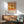 May include: Framed vintage-style poster with orange and cream background featuring detailed dragonfly illustration and Japanese text, displayed above mid-century wooden sideboard with white ceramic lamp in modern living room setting with sage green upholstered chair and round wooden coffee table