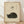 May include: Framed vintage-style poster with cream textured background featuring minimalist black illustration of sleeping cat curled in ball, Japanese calligraphy characters above, displayed against white wall on light wood floor with natural lighting and shadows