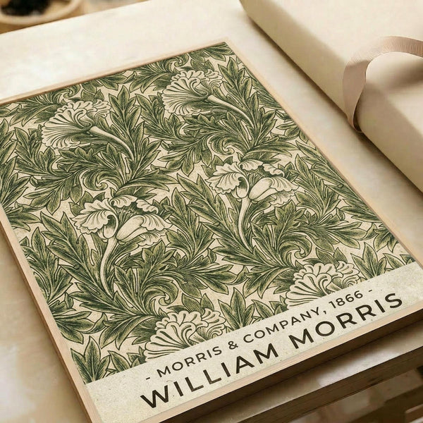 Vintage botanical print featuring intricate green acanthus leaf pattern on cream background. The detailed Art Nouveau-style design shows flowing, ornate foliage with curving stems and decorative flourishes. Print appears mounted on white paper with "MORRIS & COMPANY 1866" and "WILLIAM MORRIS" text at bottom. Cream ribbon and neutral surfaces visible in background, giving the artwork an elegant, classic appearance.