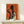 May include: Framed art print with orange textured background featuring black silhouette of elegant woman holding wine glass and smaller illustrated woman also with wine glass, displayed on light wood console table next to wrapped white gift box with natural greenery accent against white wall