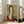 May include: Framed art print featuring a portrait of a woman with black hair and elongated neck wearing a deep red garment, painted in modernist style with muted earth tones and sage green background. Large rectangular frame leans against white wall next to beige upholstered chair in bright room with tall windows.
