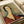 A reproduction of Modigliani's distinctive portrait style showing a woman with an elongated neck, dark bobbed hair, and almond-shaped eyes wearing a rust-colored dress against a muted green-gray background. The print displays the artist's signature elongated proportions and simplified facial features. The artwork is shown as a flat print on cream paper with visible texture and aging effects, positioned at an angle with white paper and ribbon visible in the background.