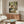 May include: Degas ballet painting reproduction displayed above walnut credenza in modern living room with white curved chair, glass coffee table, and contemporary lighting. The artwork shows dancers in white tutus with green sashes in an ornate practice room with tall windows and columns.