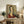 May include: Framed portrait print displayed on rustic wooden sideboard in neutral living room. Artwork shows woman with elongated face, black hair, and burgundy V-neck top in Modigliani's distinctive style with muted earth tones. Scene includes cream upholstered chair, fern plant, ceramic vase, stacked books, and soft natural lighting creating warm shadows on white walls.