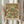 May include: Person holding framed poster featuring William Morris floral pattern with red roses, green leaves, and cream background in Arts and Crafts style. Light wood frame against soft neutral curtained background with dried pampas grass visible on left side. Vintage botanical wallpaper design from Morris & Company 1866.