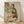 May include: Framed reproduction of an expressionist artwork showing two embracing figures in muted earth tones of green, brown, and orange against a beige background. The wooden frame sits on light hardwood flooring against white walls with natural sunlight casting diagonal shadows across the scene.