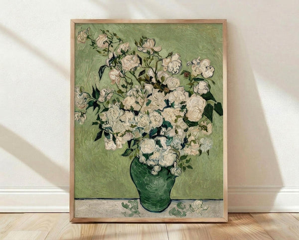 May include: Framed reproduction of Van Gogh's white roses painting in green glass vase against pale green background, displayed in light wooden frame leaning against white wall on natural wood floor with soft window light creating shadows