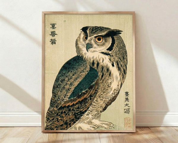May include: Framed vintage Japanese woodblock print of an owl with detailed brown and teal feathers, large orange eyes, and Japanese calligraphy on cream background. Light wood frame leaning against white wall on wooden floor with soft natural lighting casting shadows.