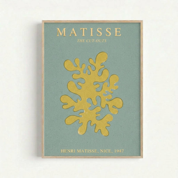 Framed art print featuring a golden yellow abstract coral or seaweed-like form against a sage green background. The organic shape has flowing, curved branches with rounded ends. Text at top reads "MATISSE THE CUT-OUTS" and bottom shows "HENRI MATISSE, NICE, 1947" in gold lettering. The print is displayed in a light wood frame against a white wall, showing the museum poster aesthetic of Matisse's famous paper cut-out artwork period.