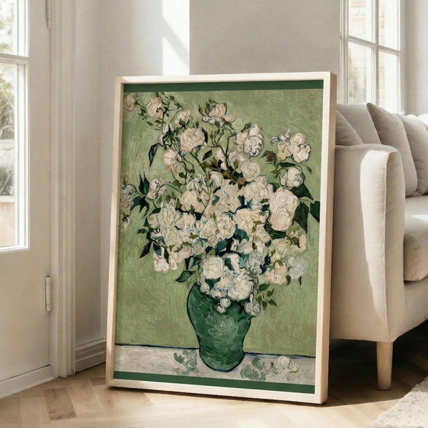 May include: Framed reproduction of Van Gogh's white roses painting displayed in bright living room. Green vase holds abundant white blooms with thick brushstrokes against sage green background. Light wood frame leans against white wall near beige armchair and large windows with natural light streaming across hardwood floors.