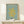 May include: Framed Matisse poster with yellow coral-like abstract cut-out shape on sage green background, displayed on light wood console table with small white wrapped gift box beside it, against cream wall with natural lighting