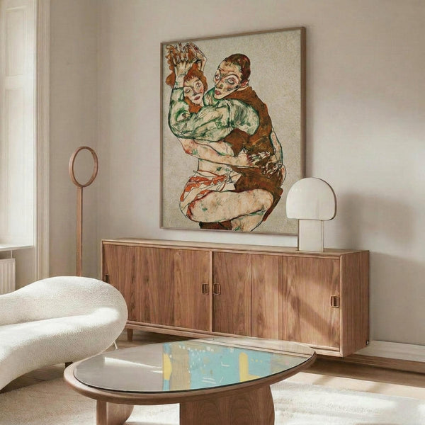 May include: Framed reproduction of early 20th century expressionist artwork showing two embracing figures in earth tones and greens, displayed above a mid-century modern walnut credenza. Room features cream walls, white upholstered chair, glass coffee table, and warm natural lighting creating shadows across the wooden furniture.