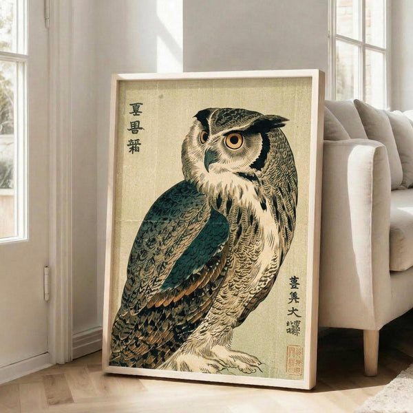 May include: Framed vintage Japanese woodblock print of an owl with detailed brown, teal, and cream feathers displayed in a bright living room. The owl has large golden eyes and intricate plumage against a beige background with Japanese text. The artwork leans against a white wall near a beige armchair and large windows with natural sunlight streaming in.