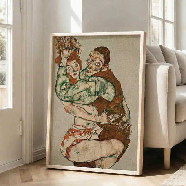 May include: Framed art print leaning against white wall next to beige sofa in bright living room. Print shows expressionist-style drawing of two embracing figures in earth tones - greens, browns, oranges - with distinctive angular faces and intertwined bodies. Light wood frame, large scale artwork positioned on wooden floor near windows.