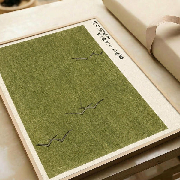 Japanese woodblock print with olive green background featuring three stylized bird silhouettes in darker green ink. Traditional calligraphy characters appear in the upper right corner on cream-colored paper with natural texture. The print is displayed in an open book or portfolio with beige pages, showing the artwork's placement within bound collection materials.