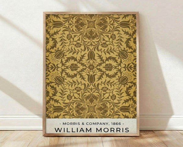 May include: Framed poster print featuring an ornate Victorian-style botanical pattern in golden yellow and brown tones, displayed against white fabric backdrop on wooden floor. The intricate design shows symmetrical floral motifs with detailed leaves, flowers, and decorative elements. White text at bottom reads "Morris & Company, 1866" and "William Morris" in black letters.