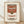 May include: Framed poster print of Campbell's condensed tomato soup can in Andy Warhol pop art style, featuring red and white label with vintage typography, displayed in thin wooden frame leaning against white wall on light wood floor with natural shadows