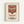 A framed print of a Campbell's condensed tomato soup can in the iconic pop art style. The artwork features a red and white soup can with "Campbell's" in white script lettering on the red upper portion and "TOMATO SOUP" in red text on the white lower portion. The print has a vintage, slightly weathered appearance and is displayed in a simple light wood frame against a white wall.