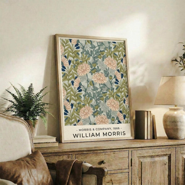 May include: Framed botanical poster with pink chrysanthemums, green foliage, and blue accents on light background, displayed on rustic wooden sideboard next to fern plant, books, ceramic vase, and brown leather chair in warm-toned living room setting with natural lighting.